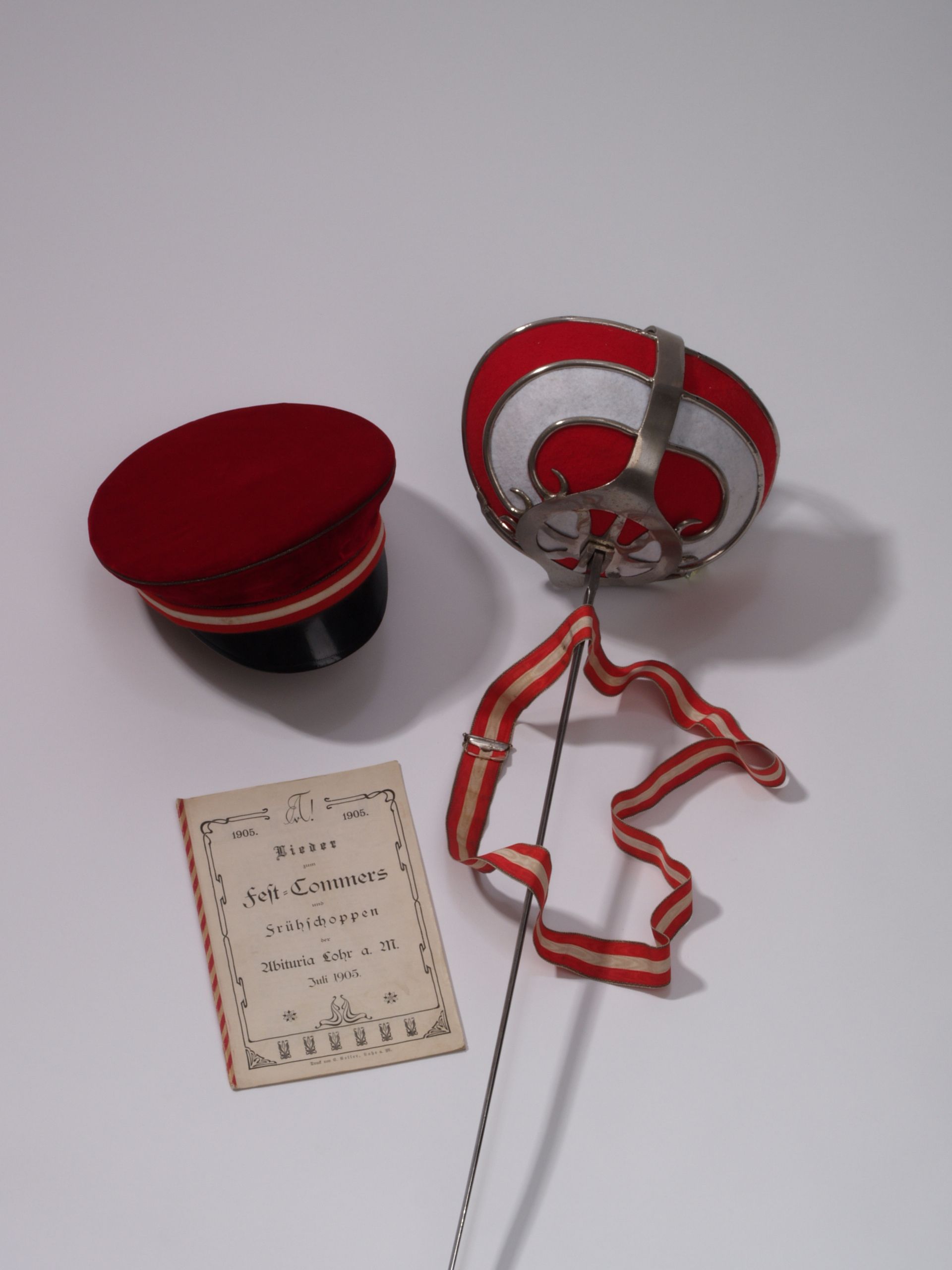 Paradeschlger (Degen), Mtze (aus "Seidensamt"), Couleurbrustband und Liederheft der Lohrer Abituria 1905 in den "Verbindungsfarben" rot-wei-rot