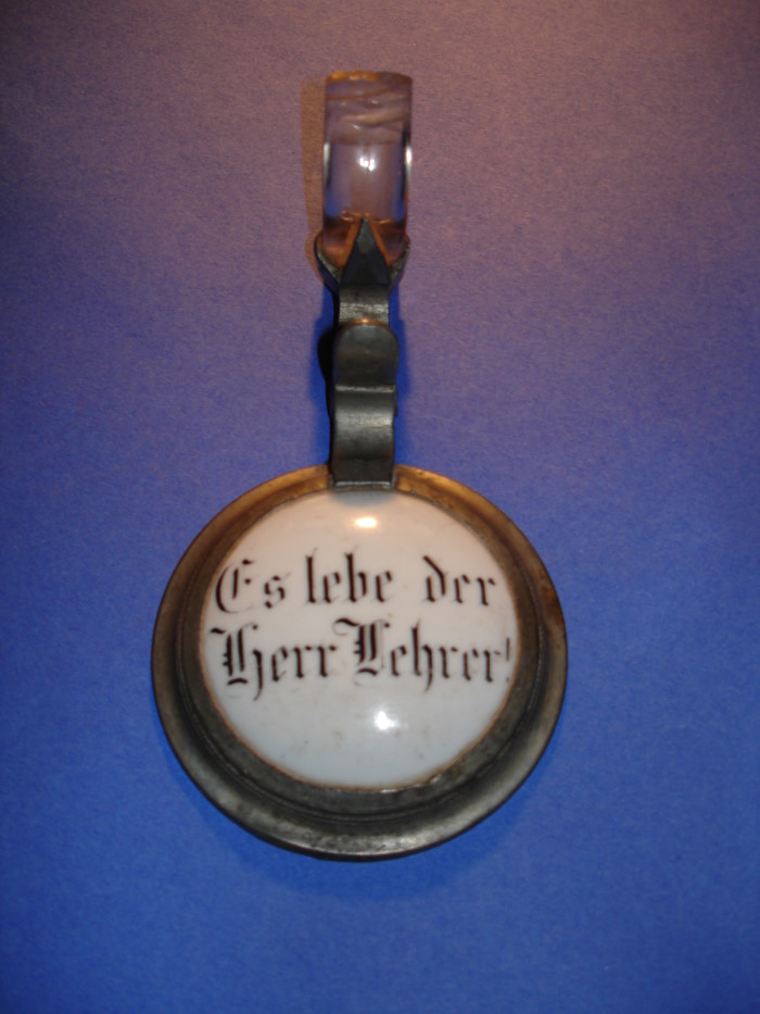 Bierkrugdeckel (um 1900) mit der Aufschrift: „Es lebe der Herr Lehrer!“ – eine ungewhnliche Ehrung fr den betreffenden Lehrer. Unabhngig von den boshaften Attacken konservativer Kreise gegen den Lehrerstand genossen viele Lehrer, vor allem auf dem Lande, hohes Ansehen. Viele Vereinsgrndungen und drfliche  Modernisierungsmanahmen wurden durch Lehrer auf den Weg gebracht. (Aus der stndigen Ausstellung des Lohrer Schulmuseums; Foto: Eduard Stenger, Schulmuseum Lohr)